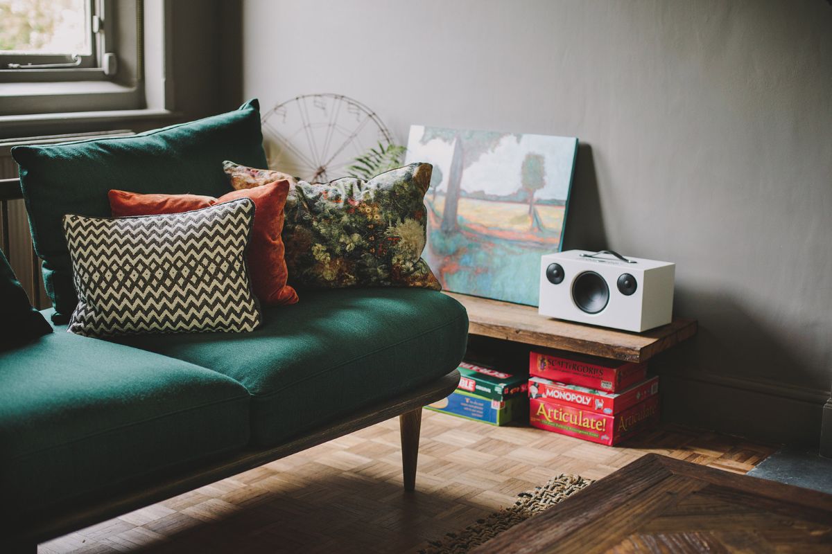 Audio Pro C10 kabelloser Lautsprecher in Weiß im gemütlichen Wohnzimmer mit grünem Sofa und bunten Kissen